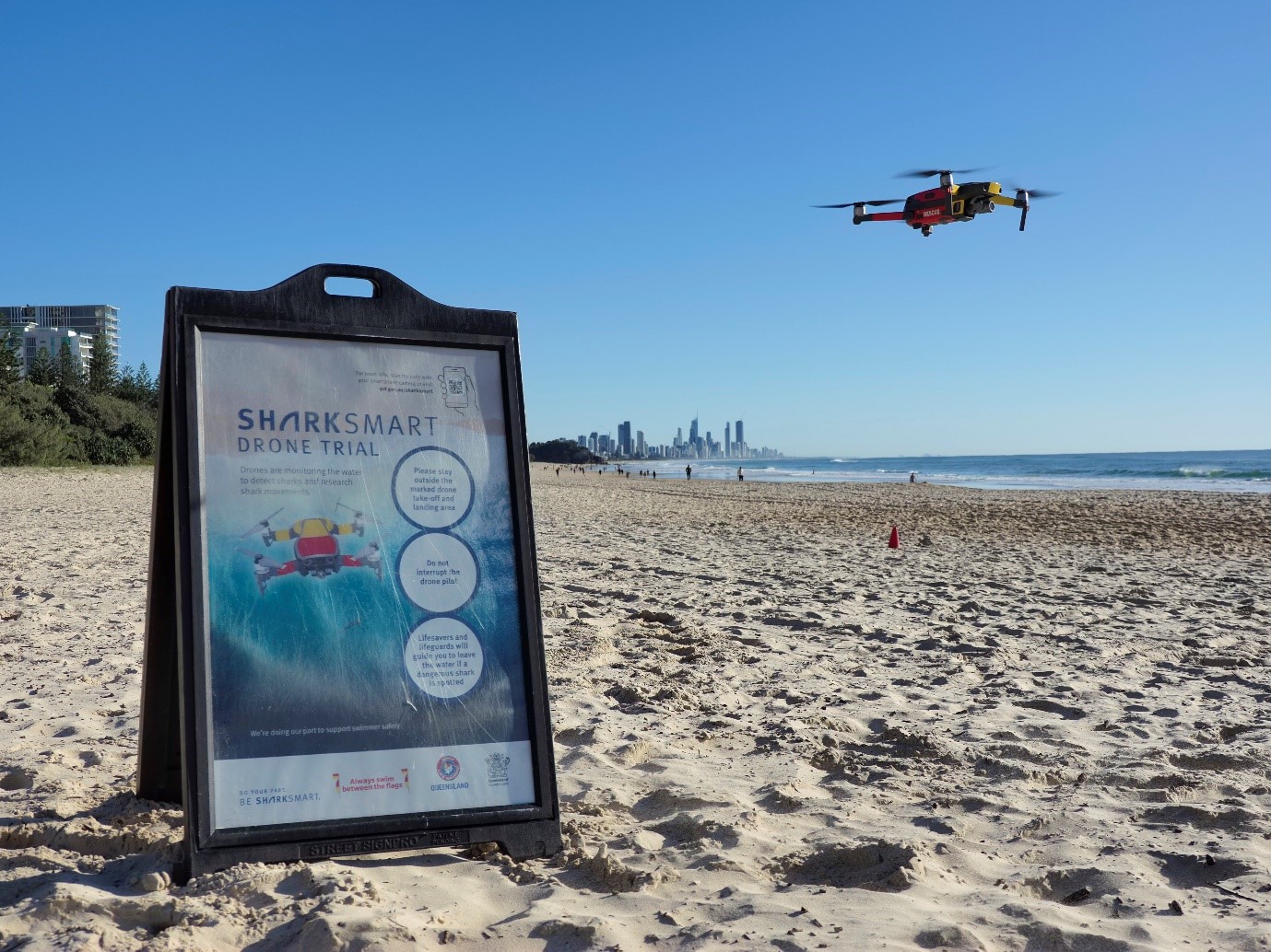 Sign on beach telling people drone trial in progress. Drone in background.