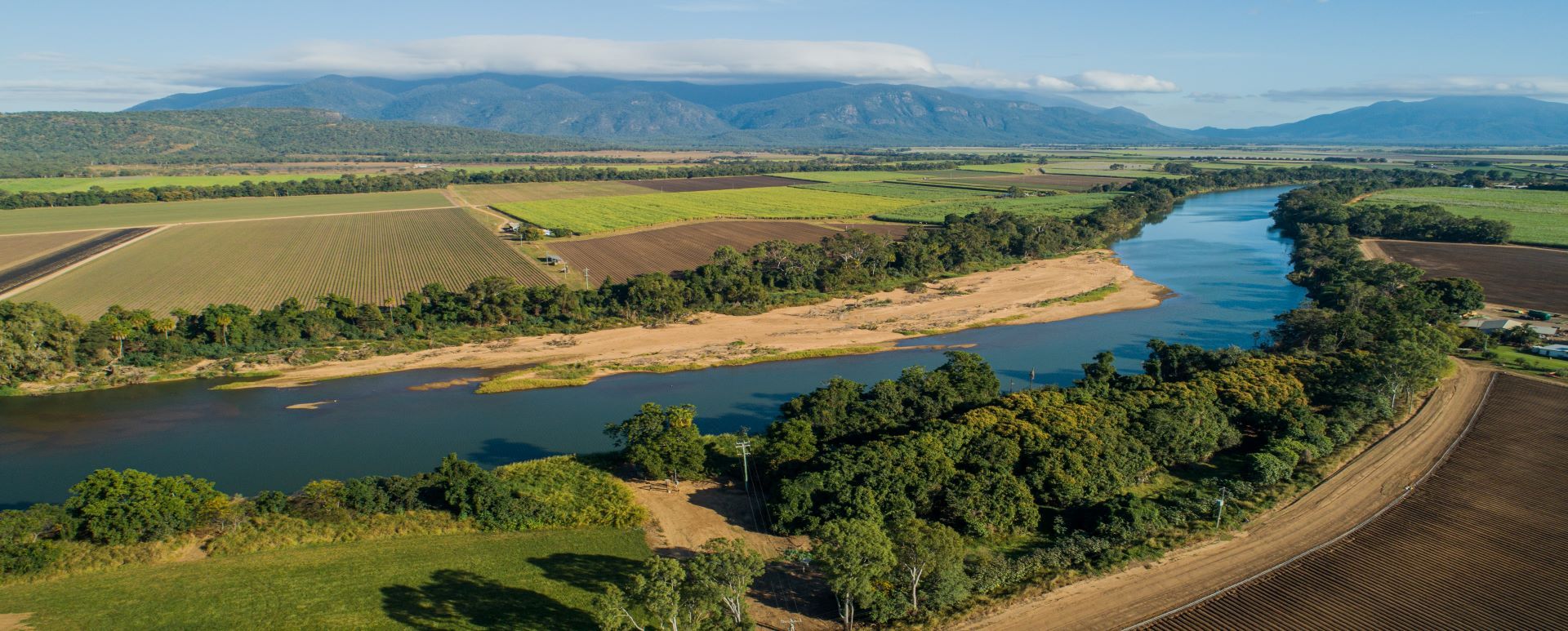 Aerial photograph of river and surrounding farmlands, with mountains in the background.