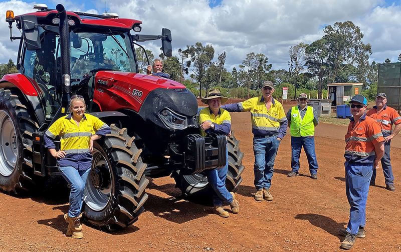 Group of seven people in high-viz clothing posing at a red tractor