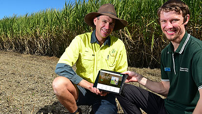 Two men sitting in a paddock, holding an iPad