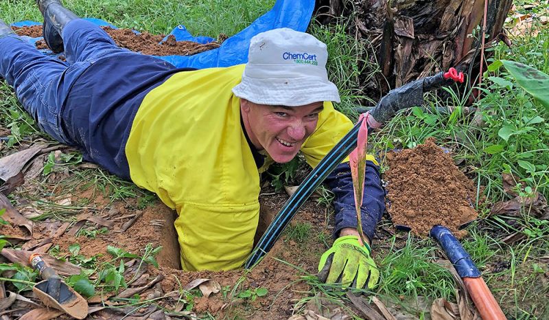 Man on stomach with his arm in a hole in the ground
