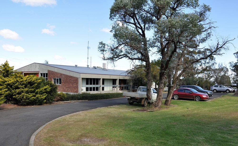 Image of low-set building, lawn and parking area