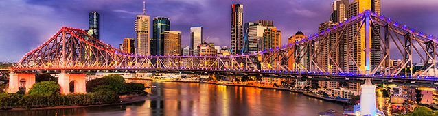 Photograph of Story Bridge in Brisbane, at dusk, with river in the foreground and highrise buildings in the background.